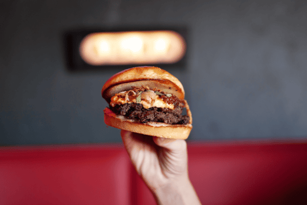 hand holding stacked cheeseburger with melted cheese and toasted bun at Smith's Olde Bar Atlanta casual bar dining
