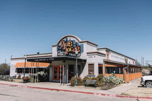 OjOs Locos Sports Cantina exterior with orange awnings and signage reading tacos, cerveza y wings under blue sky