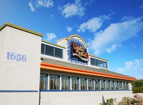 OjOs Locos sports cantina exterior at 1656 with orange trim and blue accents under a bright blue sky