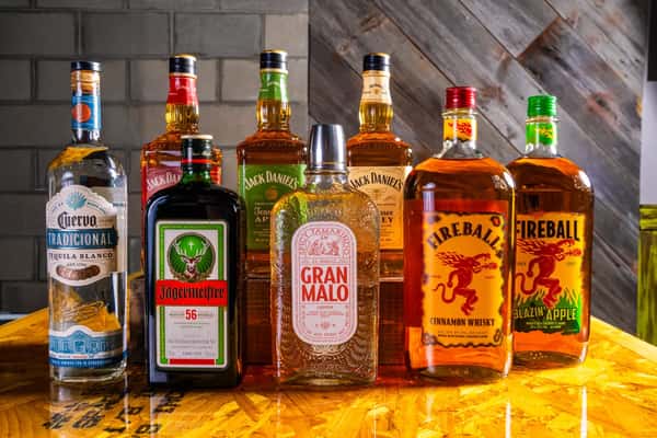 Assorted liquor bottles including Jose Cuervo, Jack Daniel's, Jägermeister, Gran Malo, and Fireball on a wooden bar counter