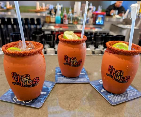Three micheladas in clay mugs with chili rims and lime wedges at Ojos Locos Sports Cantina bar.