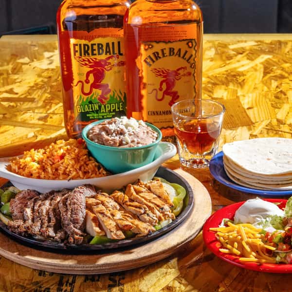 Sizzling steak and grilled chicken fajitas with rice, beans, tortillas, salad and Fireball whiskey bottles on table