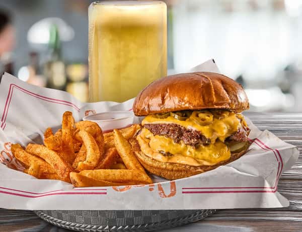 Cheeseburger with melted cheddar and jalapeños, seasoned fries, and a tall draft beer on a wooden table