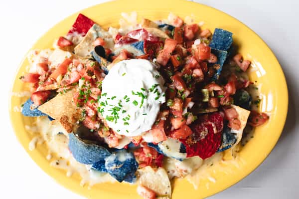 Colorful nachos topped with melted cheese, diced tomatoes, and a generous scoop of sour cream with chives, served on a yellow plate.
