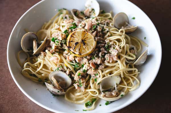 Linguine pasta with clams, chopped seafood, grilled lemon, and fresh herbs.