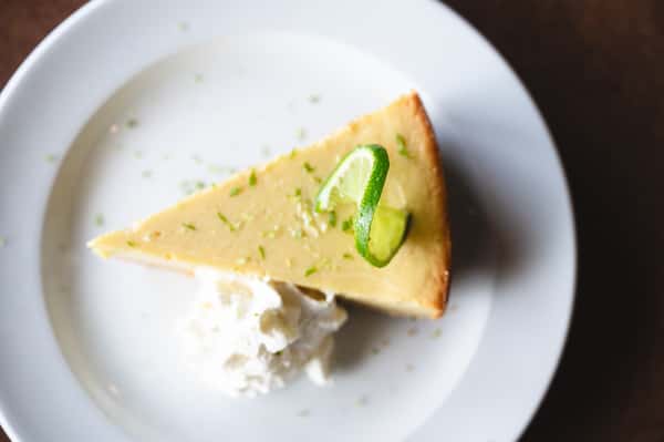 Slice of key lime pie with whipped cream and a lime twist on a white plate.