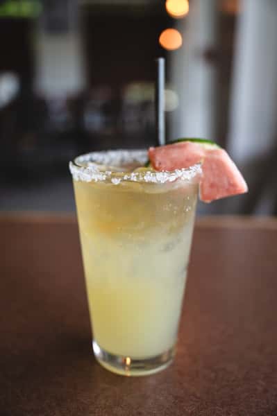 Refreshing yellow cocktail with salt rim, garnished with watermelon and lime slice.