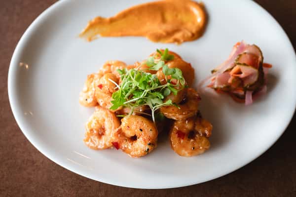 Spicy grilled shrimp with microgreens and a smear of red pepper aioli on a white plate.