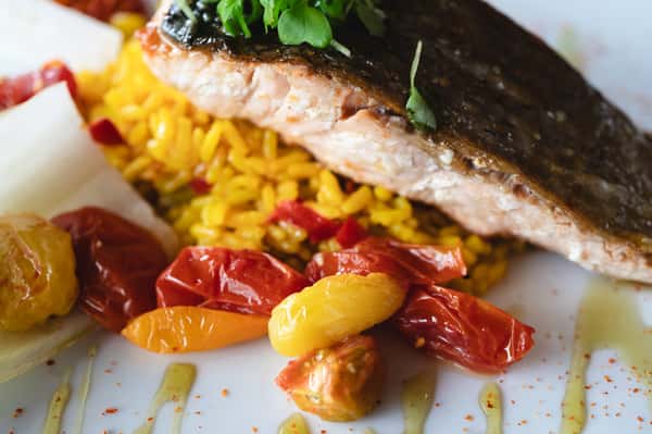 Grilled salmon served over saffron rice with cherry tomatoes and microgreens.