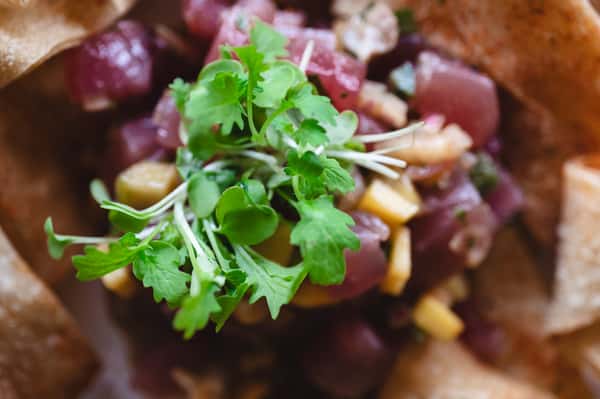 Tuna poke with mango, herbs, and tortilla chips served in a white bowl.