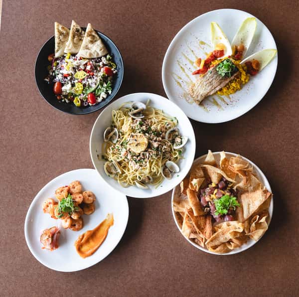 Overhead view of assorted restaurant dishes including pasta, fish, shrimp, salad, and nachos.