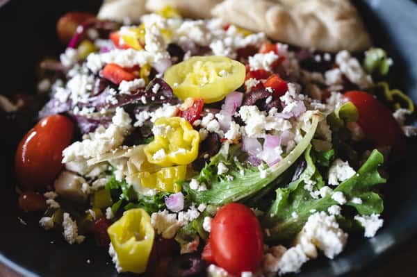 Close-up of Greek salad with colorful vegetables, feta, and pepperoncini slices.