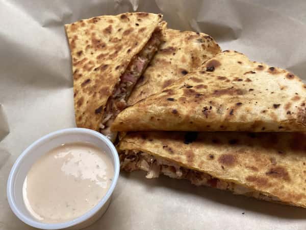 Grilled quesadilla filled with seasoned meat served with a creamy dipping sauce on parchment paper