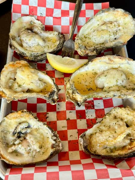 Baked oysters with garlic butter and herbs served with lemon on a red checkered tray at a seafood and BBQ restaurant
