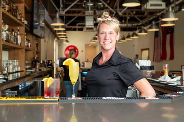 A smiling staff member serving a colorful cocktail drink at North Georgia BBQ restaurant bar area