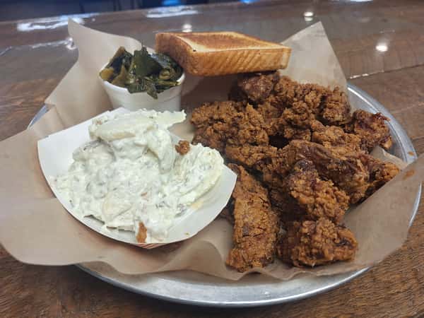 Crispy fried chicken livers served with collard greens, toast, and a side of creamy potato salad on a metal tray