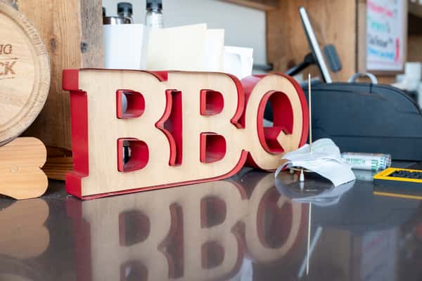 Large red BBQ letters displayed on a dark surface with their reflection visible, decorative interior signage at North Georgia BBQ restaurant
