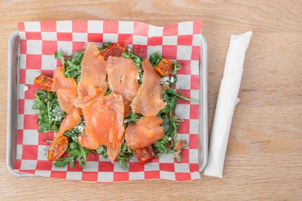 Smoked salmon slices served with fresh mixed greens on red and white checkered paper in a metal tray at North Georgia BBQ restaurant