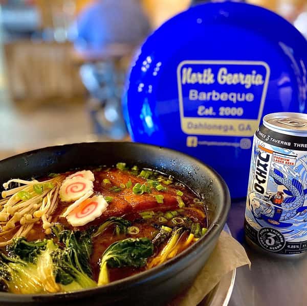 Rich ramen bowl with pork, greens, and fish cake served beside a beer at North Georgia Barbeque in Dahlonega GA