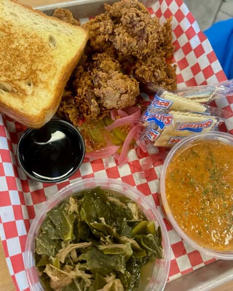 Southern-style fried chicken plate with crispy golden chicken pieces, toasted white bread, collard greens, creamy side dish, pickles, crackers, and dipping sauce on a red checkered tray