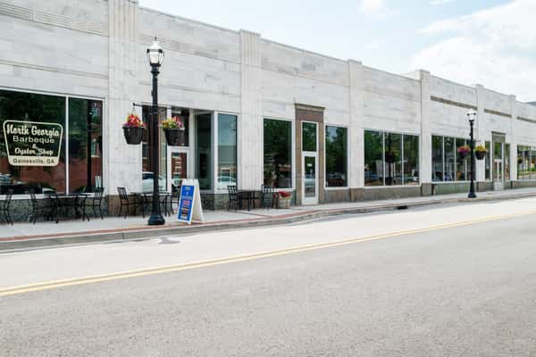 Exterior view of North Georgia BBQ restaurant showing a white commercial building with large green-framed windows, a black street lamp with hanging flower basket, outdoor seating, and a sidewalk