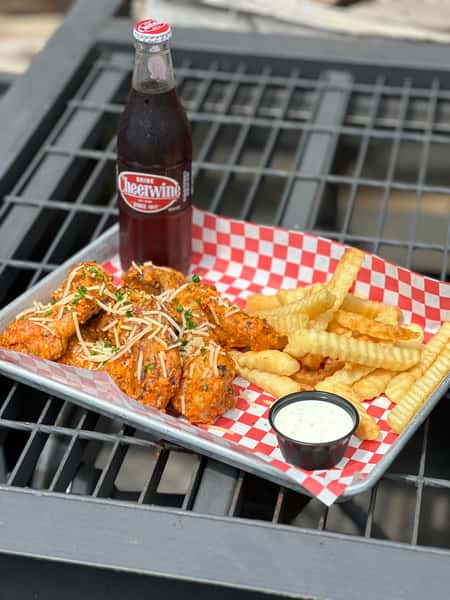 Buffalo chicken wings topped with shredded cheese served with crinkle fries and dipping sauce alongside a glass bottle soda