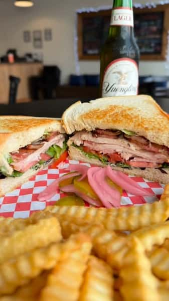 Turkey club sandwich with lettuce and tomato served with crinkle fries and beer at a casual American restaurant