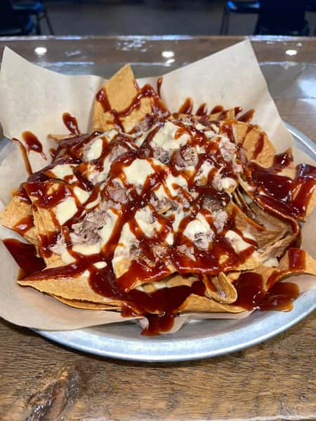 Barbecue pulled pork nachos drizzled with sauce and queso on crispy tortilla chips