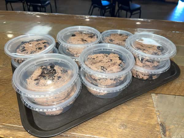 Individual chocolate dessert cups with cookie crumble topping in clear takeout containers on a tray