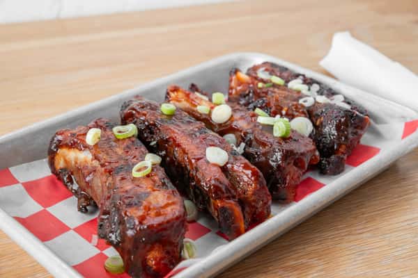 Sticky glazed BBQ ribs with green onion garnish served in a metal tray on red and white checkered paper at North Georgia BBQ restaurant
