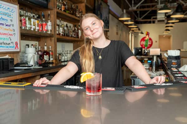 A staff member at the bar area of North Georgia BBQ restaurant preparing a cocktail with liquor bottles displayed in the background