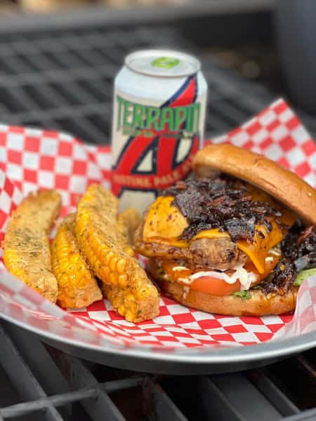 Cheeseburger with caramelized onions and melted cheddar served with grilled corn and a canned beer on a tray