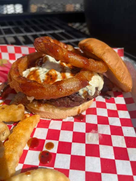 Juicy cheeseburger with crispy onion rings and barbecue sauce on a toasted bun served with seasoned fries