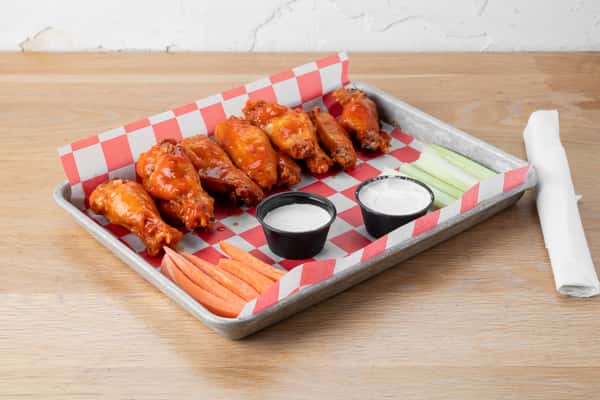 Buffalo-style chicken wings served in a metal tray with dipping sauce, carrot sticks, and celery sticks on red and white checkered paper at a restaurant