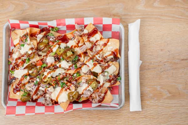 Pork nachos loaded with BBQ pulled pork, toppings, and garnishes served on red and white checkered paper at North Georgia BBQ restaurant