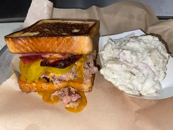 Stacked smoked pork sandwich with melted cheese and pickles served with a side of creamy potato salad