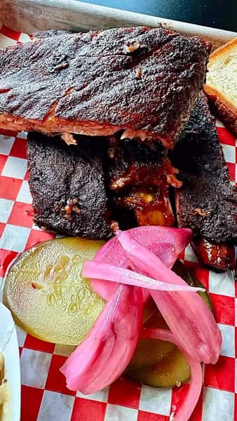 Smoked barbecue ribs with pickles and pickled onions served on a red checkered tray at a Southern BBQ spot
