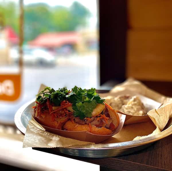 Loaded barbecue sandwich topped with slaw and fresh herbs served on a tray by a window in a casual BBQ spot