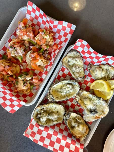 Charbroiled oysters topped with garlic butter and herbs served with lemon wedges on a seafood restaurant tray