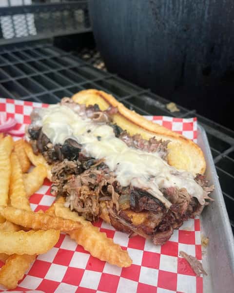 Loaded pulled pork hoagie topped with melted cheese served with crinkle fries on a red checkered tray
