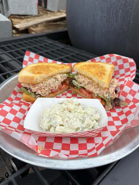 Toasted tuna salad sandwich with lettuce and tomato served with a side of creamy potato salad on a checkered tray
