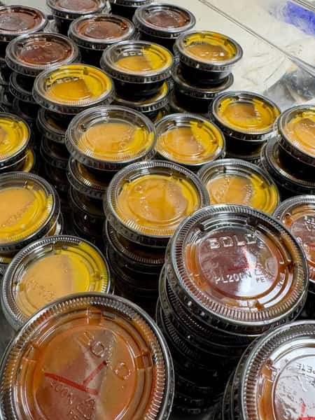 Stacked takeout sauce containers filled with house-made barbecue and dipping sauces, ready for restaurant to-go orders