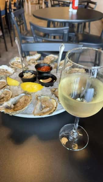 Fresh raw oysters on the half shell with lemon and sauces served with white wine at a seafood restaurant