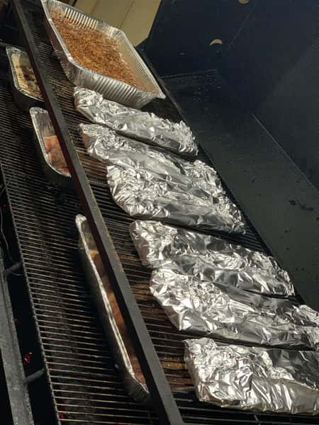 catering trays on a grill with meat wrapped in foil