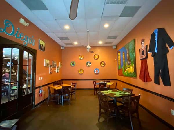 Warm and inviting Mexican restaurant dining room with orange walls, wooden tables, decorative wall art, and traditional cultural accents near Diego's dining area.