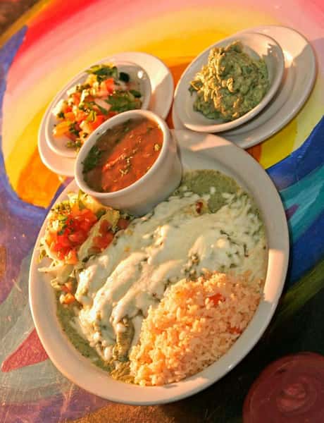 Chicken enchiladas verdes topped with melted white cheese and creamy green salsa, served with Mexican rice, pico de gallo, red salsa, and fresh guacamole – authentic Mexican restaurant dinner plate.