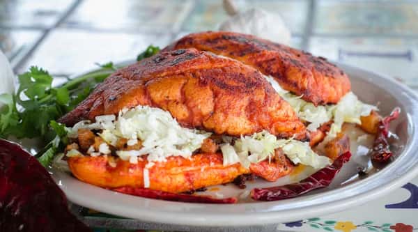 Grilled Mexican pambazo sandwich filled with chorizo and potatoes, topped with shredded lettuce and queso fresco, served with dried red chilies and fresh cilantro – authentic Mexican street food specialty.