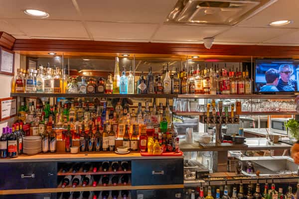 Fully stocked bar at Sindbad's Restaurant, featuring a wide selection of spirits, wine, and beer taps, with a flat-screen TV and open kitchen view — perfect for casual drinks and social gatherings.