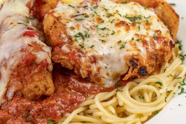 Close-up of crispy chicken Parmesan topped with melted mozzarella and marinara sauce, served over a bed of al dente spaghetti and garnished with fresh parsley — a classic Italian-American pasta dish.