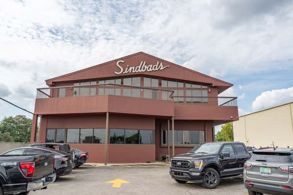Full exterior shot of Sindbad's Restaurant with red wood paneling, wraparound balconies, and onsite parking — a landmark Detroit seafood spot with riverfront views.